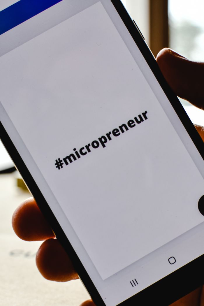 creative-03 Close-up of a hand holding a smartphone with the hashtag #micropreneur on screen, symbolizing entrepreneurship.